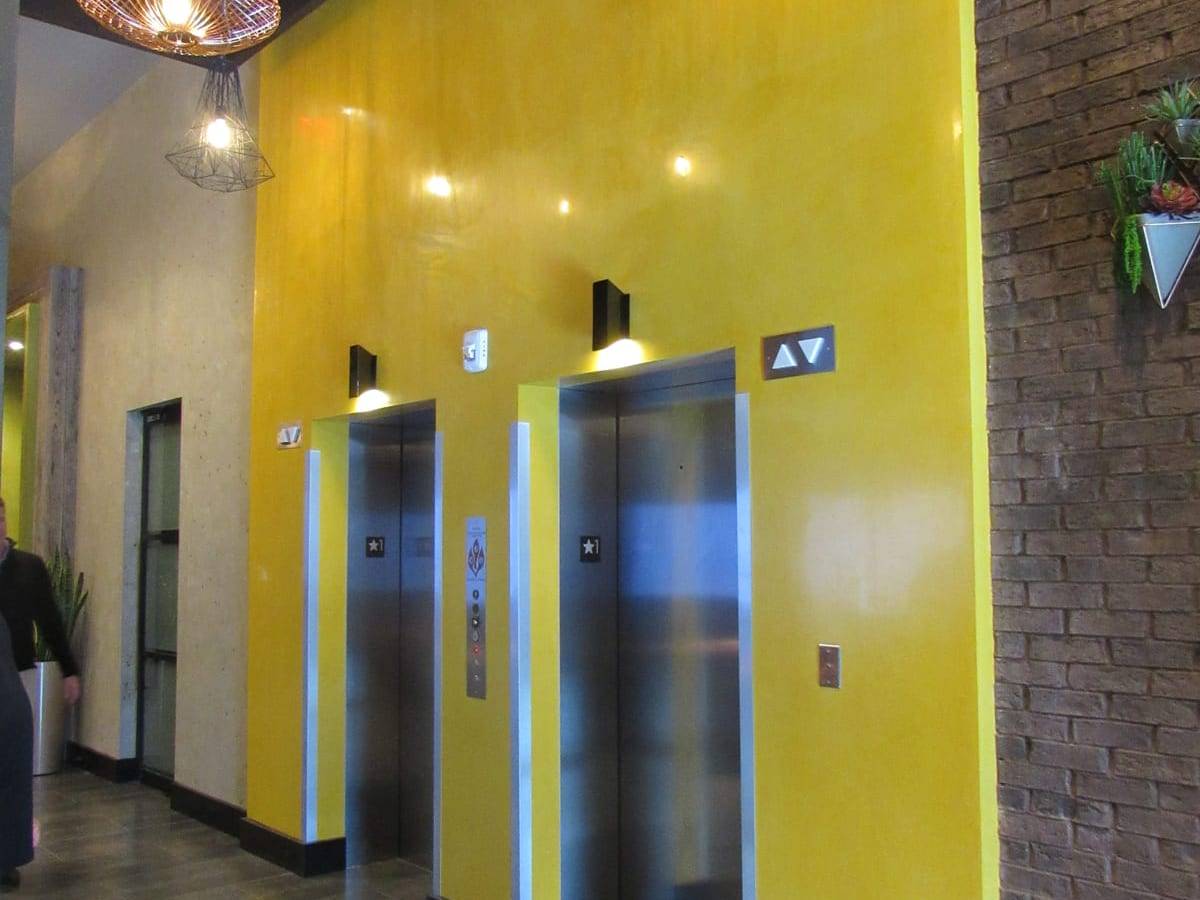 Elevator lobby with a saturated yellow Venetian plaster wall beside exposed brick
