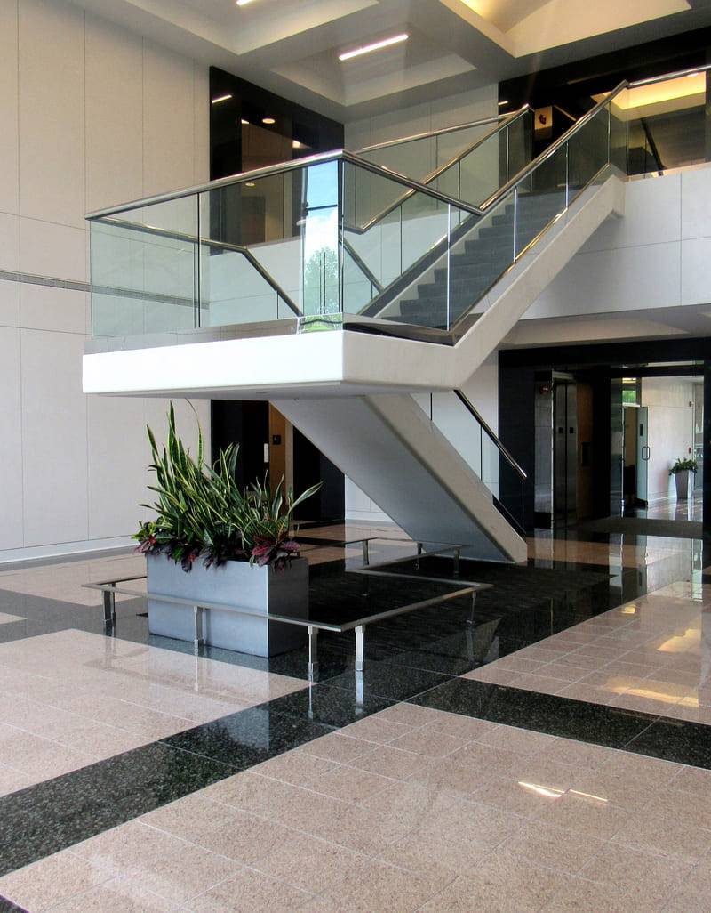 Office lobby with a glass-railed stair over polished stone and plaster surfaces