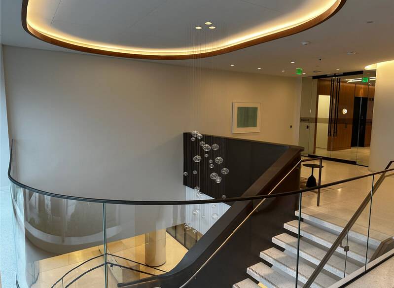 Hotel stair landing with a curved acoustic plaster ceiling above a glass balustrade